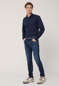Camicia a maniche lunghe blu navy, con bottoni e colletto, abbinata a jeans blu scuro. Indossata con sneakers multitexturizzate beige e bianche.