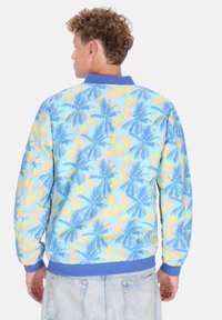 Giacca bomber leggera con un design di palme blu e pastello, con un colletto e polsini blu a tinta unita.