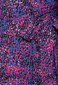 Tissu coloré avec un motif abstrait en rose, bleu, noir et blanc, présentant un détail de nœud noué sur un matériau froncé.