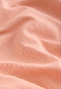 Soft, textured fabric in a light peach color, featuring gentle folds and a smooth surface. Contains a fine, even weave pattern.