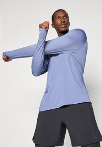 Lichtpaarse lange mouwen sportshirt met een slim fit, gecombineerd met zwarte shorts. De stof lijkt glad en rekbaar.