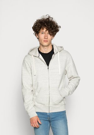 Ljusgrå zip-up hoodie med en texturerad tyg, dragsko huva och framfickor. Bärs med en svart t-shirt och blå jeans.