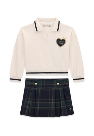 Polo blanc à manches longues avec des rayures noires et un logo en forme de cœur, associé à une jupe plissée écossaise bleu marine et verte avec des boutons dorés.