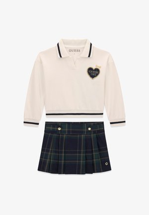Wit poloshirt met lange mouwen met zwarte strepen en een hartlogo, gecombineerd met een marineblauw en groen geruit geplooide rok met gouden knoopdetails.