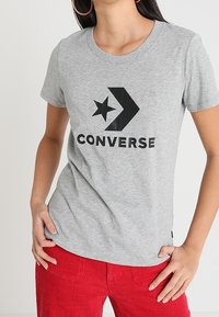 Szara bawełniana koszulka z nadrukiem czarnej gwiazdy i strzały, z napisem "CONVERSE" poniżej. Krótkie rękawy i okrągły dekolt.