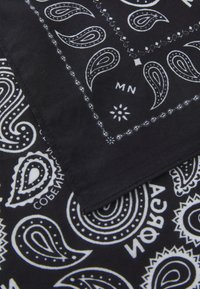 Sort bandana med hvide paisley-mønstre og geometriske elementer. Blødt bomuldsstof med syede kanter, der måler cirka 50x50 cm.