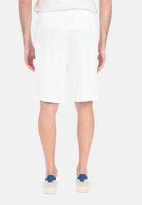 Pantaloni corti bianchi con una vita elasticizzata, taglio dritto e tessuto leggero. Indossati con sneakers beige con accenti blu.