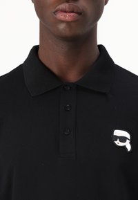 Μαύρο πόλο μπλουζάκι από βαμβάκι με τριπλό κούμπωμα και λαιμόκοψη ριμπ. Διαθέτει λογότυπο σε απόχρωση, το οποίο είναι τοποθετημένο στο αριστερό στήθος.