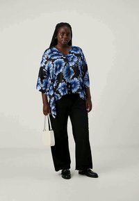 Black floral blouse with blue flowers, v-neckline, loose fit; paired with black wide-leg pants and a small white handbag. Black shoes.
