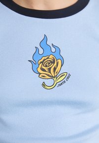 T-shirt fitted di colore azzurro chiaro con una trama a costine, con un design di rosa gialla circondata da fiamme blu e il testo "Santa Cruz".