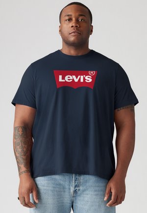 T-shirt en coton bleu marine avec un grand logo rouge Levi's sur la poitrine. Manches courtes et coupe décontractée. Porté avec un short en denim clair.