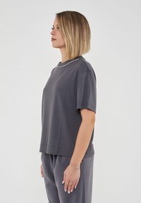 T-shirt grigio a maniche corte con una vestibilità rilassata, caratterizzato da un dettaglio sottile sul collo. Texture liscia, abbinato a pantaloni grigi in tinta.