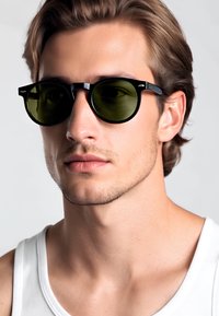 Occhiali da sole con montatura rotonda nera e lenti verdi. Le caratteristiche includono accenti in metallo sulla montatura, finitura opaca e design leggero.