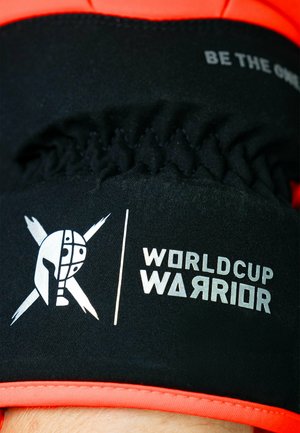Black and orange athletic gear with elastic texture. Features a stylized helmet logo and text "WORLD CUP WARRIOR" in silver.