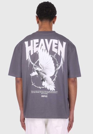 Gray oversized t-shirt featuring white graphics, including "HEAVEN," a dove, and barbed wire. Text above and below the dove contains motivational phrases.
