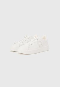 Λευκά sneakers χαμηλού ύψους με λογότυπο στην πλευρά, μπροστινό δέσιμο με κορδόνια και λαστιχένια σόλα σε απλό λευκό φόντο.