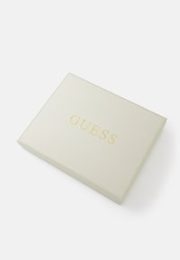 Šviesiai béžinė tekstūruoto paviršiaus stačiakampė dėžutė su auksiniu "GUESS" logotipu. Plokščias, lygus paviršius su subtiliu blizgesiu, be papildomų raštų ar akcentų.