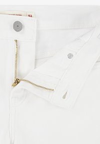 Shorts en denim blanc avec détail de fermeture éclair dorée, fermeture par bouton et étiquette visible ; le tissu est texturé et lisse avec une finition soignée.