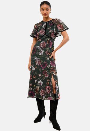 Floral dress with dark green base, short flutter sleeves, side slit, and contrasting black trim. Complemented by knee-high black boots.