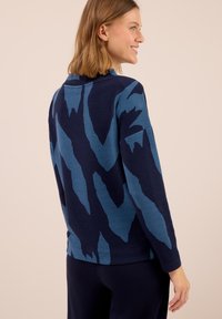 Pull à motifs bleus avec une texture en côtes et des manches longues, doté d'un col montant et d'un design audacieux dans des tons de bleu plus foncé.