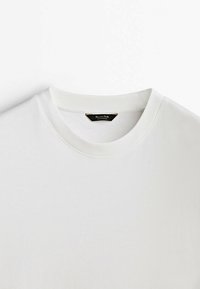 Gros plan d'un t-shirt blanc uni à col rond avec une étiquette de marque noire cousue à l'intérieur du col.