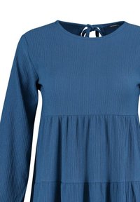 Robe bleue à manches longues texturée avec taille froncée et fermeture à nouer à l'arrière de l'encolure ronde.