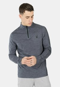 Grijze pullover met lange mouwen en een kwart-rits hals, gemaakt van textuurstof. Heeft een klein zwart spinnenlogo op de linkerkant van de borst.