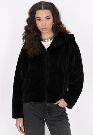 Schwarze Kunstpelz-Jacke mit Reißverschluss und Kapuze, die eine weiche Textur und eine lockere Passform hat. Kombiniert mit dunklen Jeans für einen lässigen Look.