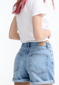 Shorts de mezclilla en azul claro con cintura alta, puños enrollados y dos bolsillos traseros. Presenta una etiqueta de cuero marrón en la cintura.