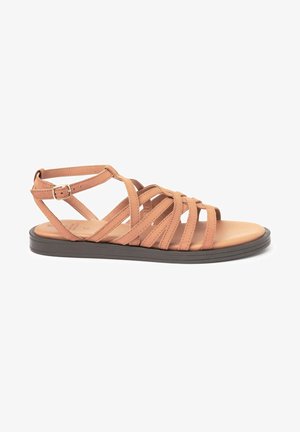 Sandale à lanières en cuir beige avec une semelle plate marron. Comprend plusieurs lanières horizontales et une boucle réglable à la cheville pour un ajustement parfait.