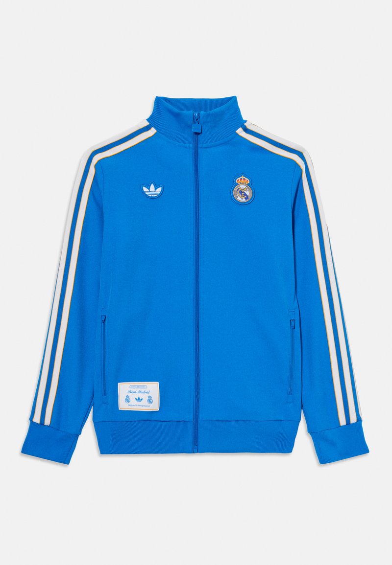 Casaco azul com fecho éclair, apresentando riscas brancas e douradas, gola alta e logos da Adidas e do Real Madrid. Fabricado em um material suave.