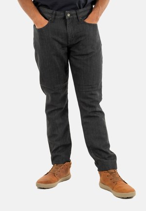 Jeans gris oscuro de corte clásico, con cinco bolsillos y cierre de botón. Combinados con botas de piel marrones con cordones y una camisa oscura.