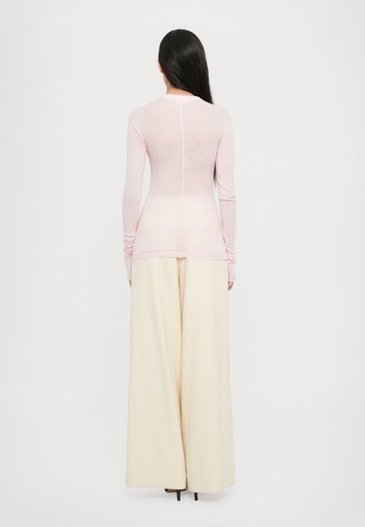 Top roz deschis cu mâneci lungi, cu un design ajustat, asortat cu pantaloni largi și fluidi de culoare crem și tocuri înalte negre. Vedere din spate.