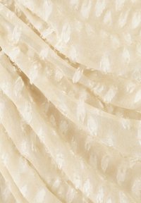 Tissu crème avec une texture douce en relief de pois disposée en plis délicats.