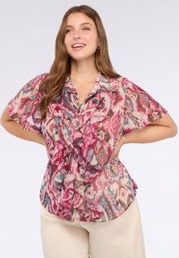 Blusa corta de manga corta y transparente con un patrón abstracto multicolor en rosa. Diseño con volantes en el frente, con cuello y cierre de botones.