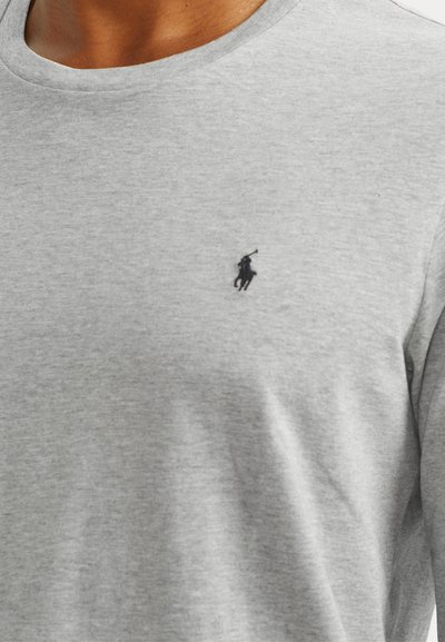 Camiseta de algodão cinza com decote redondo e gola ribana. Apresenta um pequeno logotipo preto de um jogador de polo no lado esquerdo do peito. Textura suave.