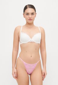 Vit spetsbehå med scallopade kanter, matchad med en rosa spetstrosa med intrikata blommönster. Släta remmar, minimal hårdvara.