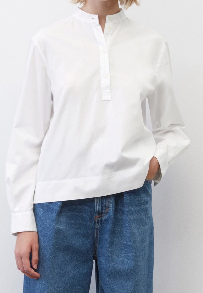Weißes Baumwollhemd mit Stehkragen, mittlerer Knopfleiste und langen Ärmeln, kombiniert mit blauen Jeans. Glatte Textur, lässige Passform.
