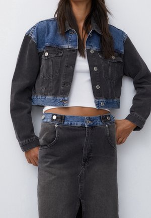 Nainen pukeutuu lyhennettyyn kaksiväriseen farkkutakkiin ja tummansävyiseen korkeavyötäröiseen farkkuhameeseen, jossa on edessä halkio, yhdistettynä valkoiseen lyhyeen toppiin.