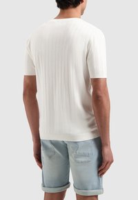 Witte geribbelde trui met korte mouwen en een ronde halslijn, gedragen met lichtblauwe denim shorts. De stof lijkt zacht en gestructureerd.