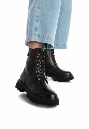 Stivaletti neri in pelle con punta rotonda, suola spessa e lacci con occhielli dorati. Indossati con jeans cropped di colore azzurro chiaro.