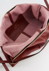 Red leather handbag with a pink suede interior. Features a zip closure, interior pocket, and adjustable straps. Gold hardware accents.