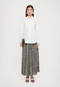 White long-sleeve shirt with a button-down collar paired with a patterned maxi skirt featuring a snake print in neutral tones and flat black sandals.