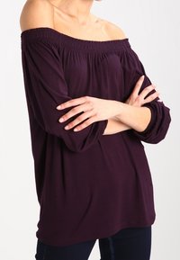 Olkapäiltä avonainen tumman violetin värinen paita, jossa on smockatut kauluskohdat, pitkät hihat kerättyine hihansuineen ja rento istuvuus.