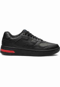 Black leather sneaker featuring perforated detailing, a flat design, and a red accent on the outsole. Lace-up closure and reinforced heel.