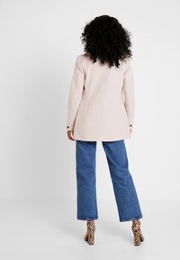 Jasnoróżowa dopasowana marynarka o sztywnym kroju, z tylnymi szwami i czarnymi guzikami, zestawiona z szerokimi niebieskimi dżinsami i szpilkami w wężowy wzór.