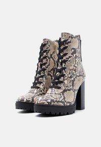 Ζευγάρι μποτάκια με ψηλά τακούνια και μαύρα κορδόνια, σε μπεζ και μαύρο σχέδιο φιδιού, με φαρδύ πάτο και πλαϊνό φερμουάρ.