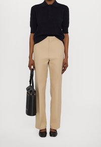 Polo a maniche corte blu navy, pantaloni beige su misura, scarpe basse nere e borsa nera con manico rotondo. Design semplice e strutturato.