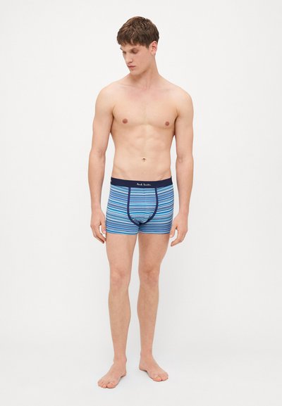 Boxers en coton avec des rayures horizontales bleues, ceinture élastique et logo affiché. Le mannequin est pieds nus et se tient debout.