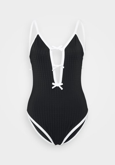 Maillot de bain une pièce noir avec une finition texturée, bord blanc, décolleté profond et détails de liens à l'avant et aux épaules.